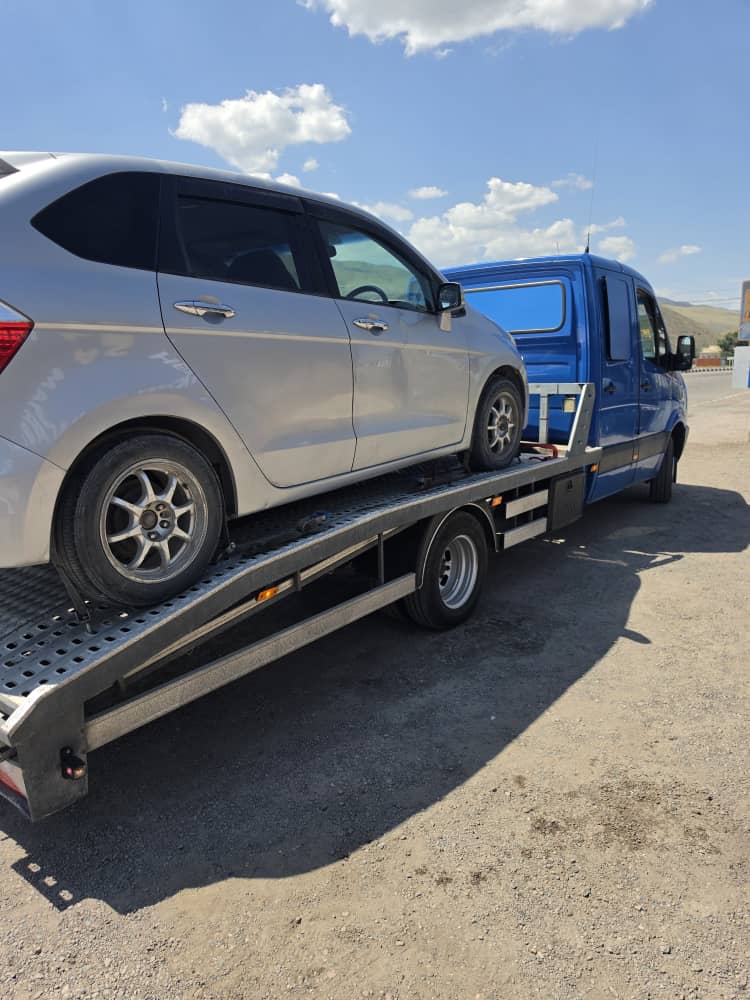 Жёлтый эвакуатор перевозит легковой автомобиль